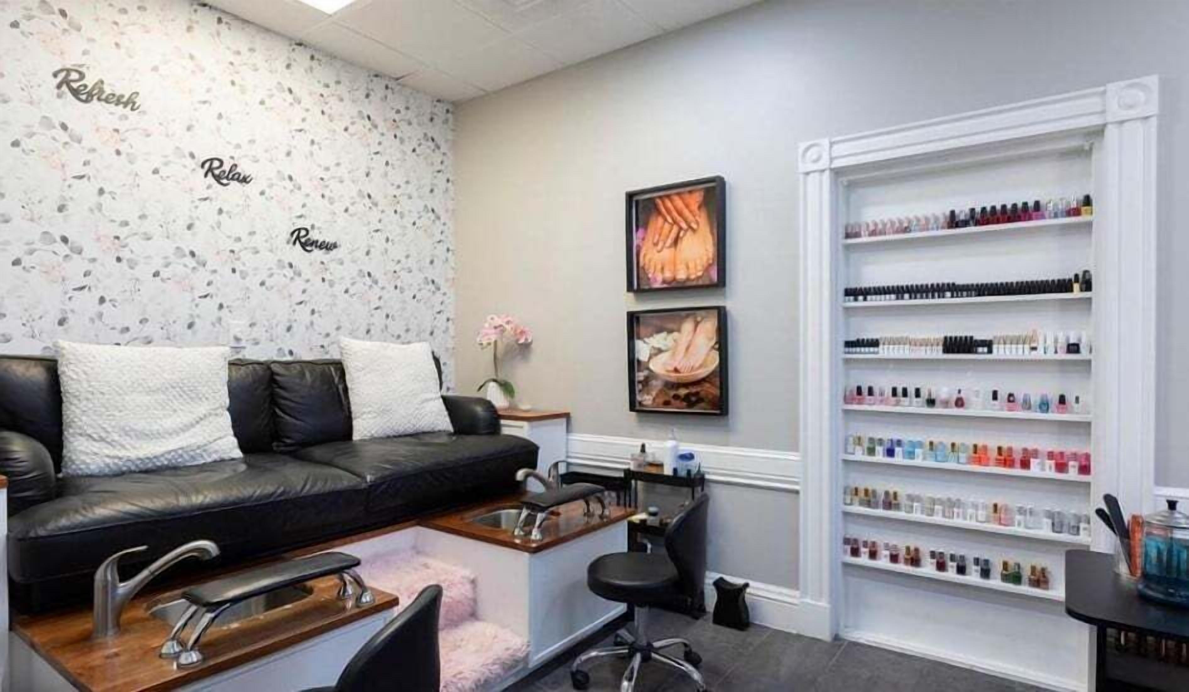 Een moderne salon met een zwarte leren bank, een kaptafel met een wastafel, en schappen vol nagellak.