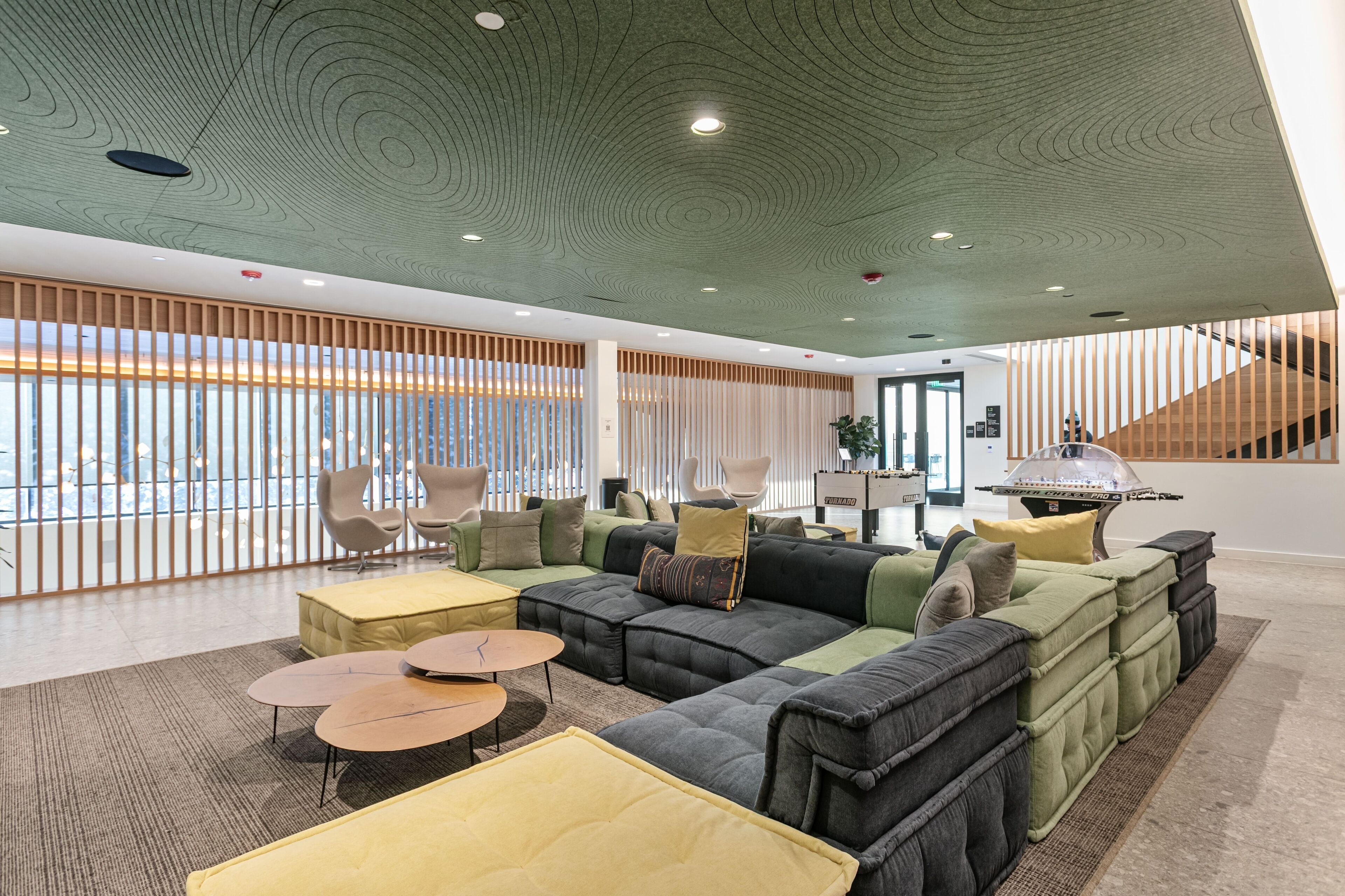 A modern lounge area with a sectional sofa, round tables, and a view of the city through large windows.