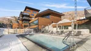 Un edificio moderno con zona de piscina, que incluye un jacuzzi y sillones de descanso.