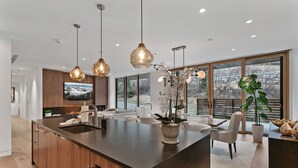 Una cucina moderna con una grande isola, luci a sospensione e vista sull'esterno grazie a ampie finestre.