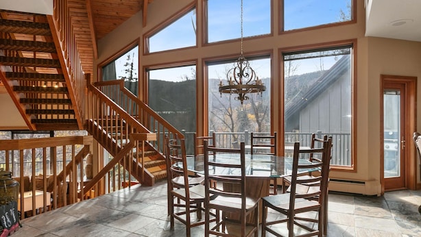 A spacious room with a large dining table, wooden chairs, a chandelier, and a staircase leading to an upper level. - Family-friendly Ski Escape With Hot Tub 4 Bedroom Condo (Park City)