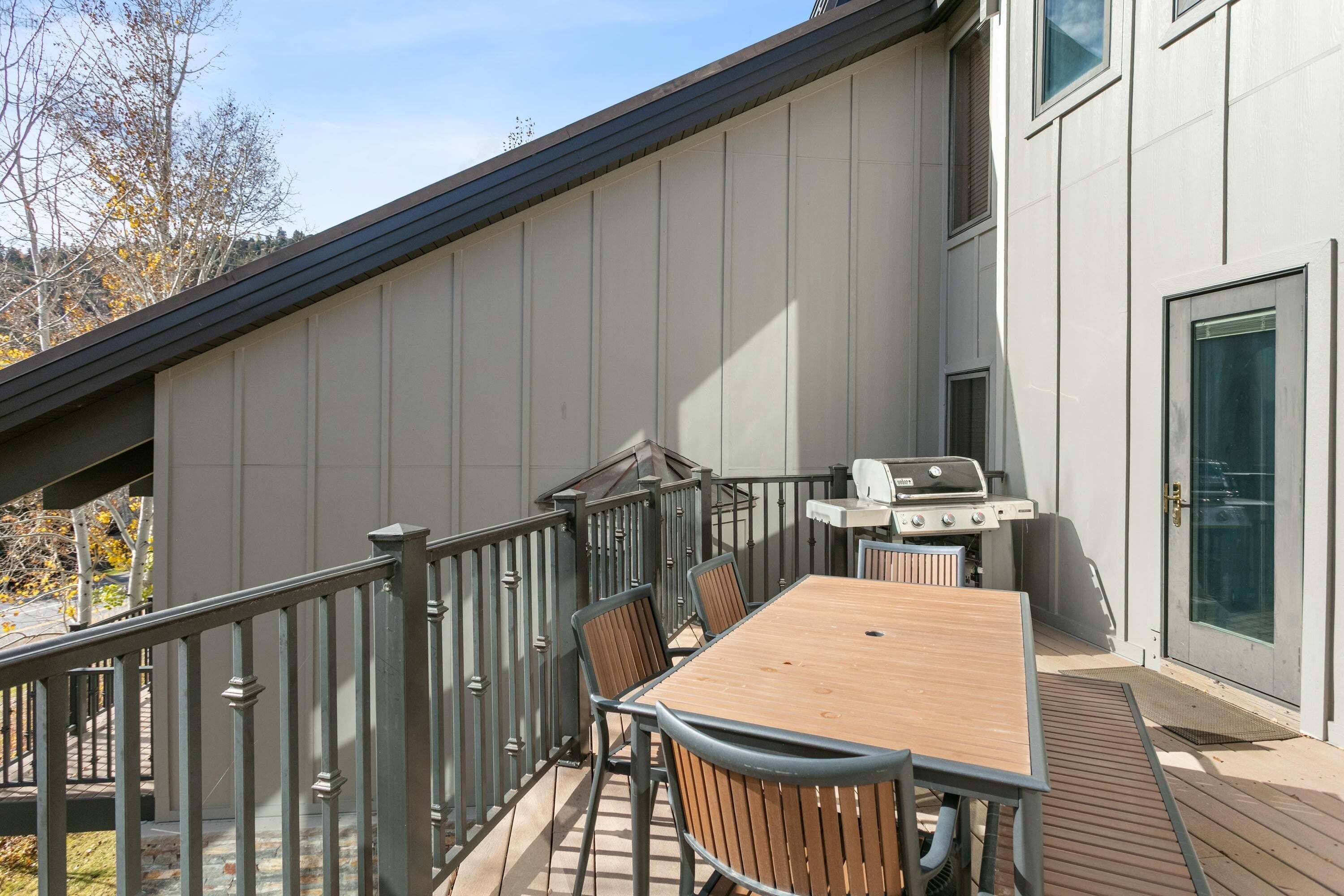 Una terraza con mesa y sillas, una parrilla y una puerta con panel de vidrio.