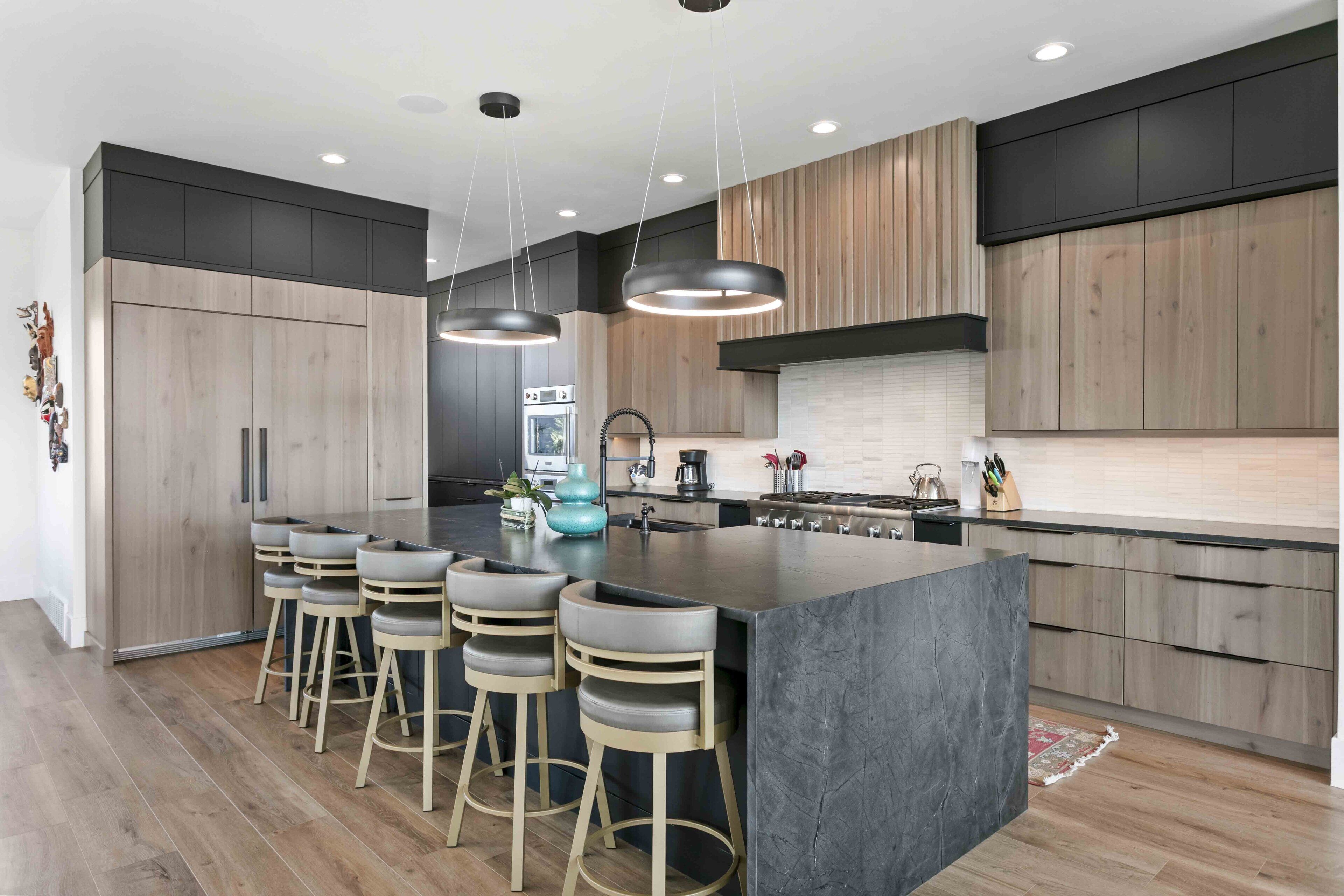 A modern kitchen with a central island, bar stools, wooden cabinets, and pendant lighting.
