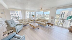 A spacious living room with a large window, a ceiling fan, and a modern sofa set. - Shoreline Towers 1116 3 Bedroom Condo (Destin)