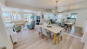 A spacious living area with a dining table, sofas, and a kitchen area with cabinets and a countertop. - Shoreline Towers 1116 3 Bedroom Condo (Destin)