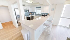 A modern kitchen with a central island, white cabinetry, and a stainless steel refrigerator. - Shoreline Towers 1116 3 Bedroom Condo (Destin)