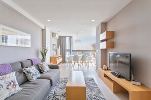 A modern living room with a grey sofa, a flat-screen TV, a wooden coffee table, and a dining area with white chairs and a glass table. - GEMELOS relax apartment (Benidorm)