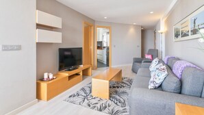 Ett modernt vardagsrum med en platt-TV, en grå soffa, ett soffbord i trä och en mönstrad matta.