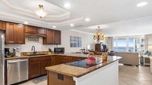 A modern kitchen with wooden cabinets, a granite countertop, stainless steel appliances, and a central island. - Shoreline Towers 1115 2 Bedroom Condo (Destin)