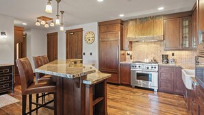 Une cuisine avec un îlot central, des meubles de rangement en bois, une horloge et une cuisinière.