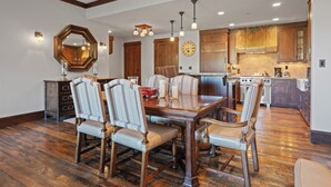 Une salle à manger avec une table en bois et six chaises rembourrées, un grand miroir et une horloge au mur.