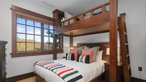 Une chambre avec un lit superposé, une grande fenêtre, une tête de lit en bois et une couverture colorée à rayures.