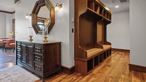 Un banc en bois doté d’un siège et d’un dossier rembourrés, un grand miroir avec un cadre hexagonal et un meuble en bois foncé, muni de tiroirs et surmonté d’une lampe.