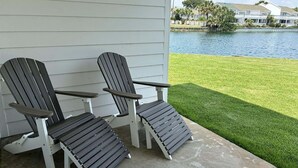 Two Adirondack chairs on a concrete patio with a view of a lake and houses in the background. - Shoreline Towers T/h 08 2 Bedroom Condo (Destin)