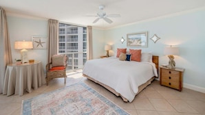 A hotel room with a bed, a chair, a table, a lamp, a ceiling fan, and a view of the outside. - Shoreline Towers 1095 2 Bedroom Condo (Destin)