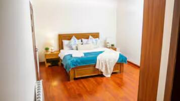 Quarto com cama de madeira, roupa de cama branca e mesa de cabeceira com abajur.