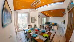 Un coin repas avec une table et des chaises en bois, un tableau accroché au mur et une vue sur l’extérieur par une fenêtre.