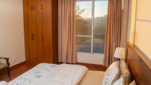 Une chambre à coucher avec un grand lit, une table de chevet, une fenêtre avec des rideaux et une armoire en bois.