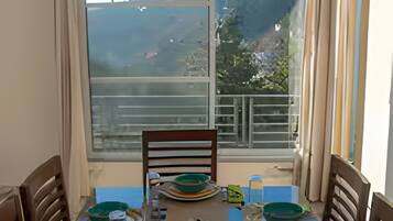 A dining area with a table set for two, a chair, and a view of a mountainous landscape through a large window.