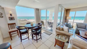 A room with a balcony, a dining table with chairs, a sofa, and a glass coffee table. - Shoreline Towers 2036 3 Bedroom Condo (Destin)