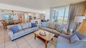 A living room with a sofa, armchairs, a coffee table, and a view of the kitchen and balcony. - Shoreline Towers 2036 3 Bedroom Condo (Destin)