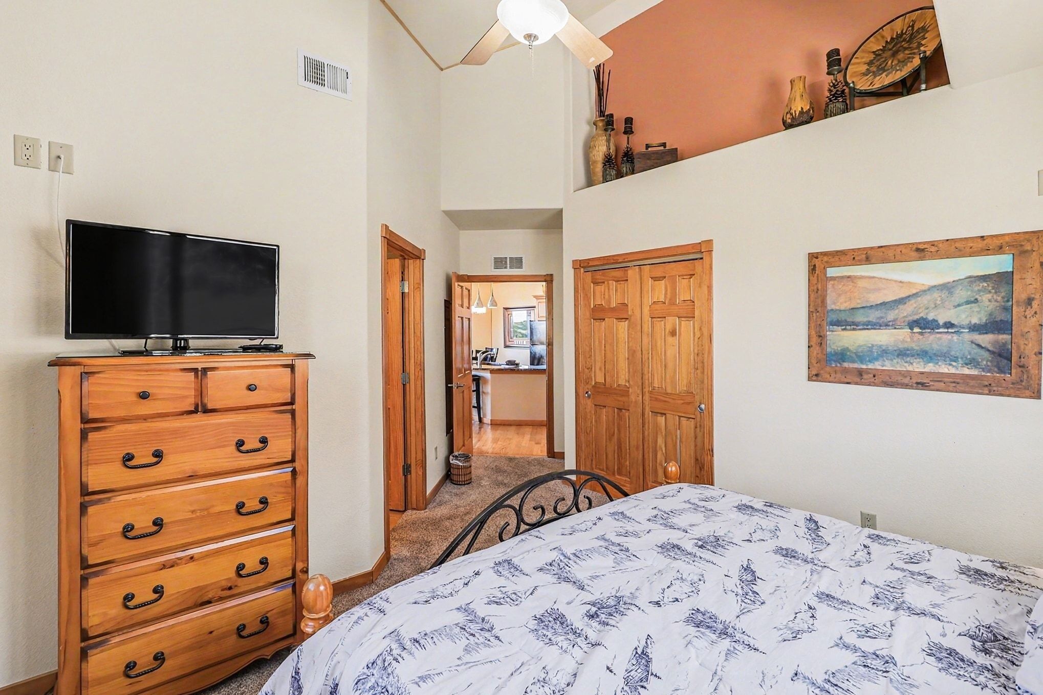 A bedroom with a bed, a dresser, a television, and a painting on the wall.