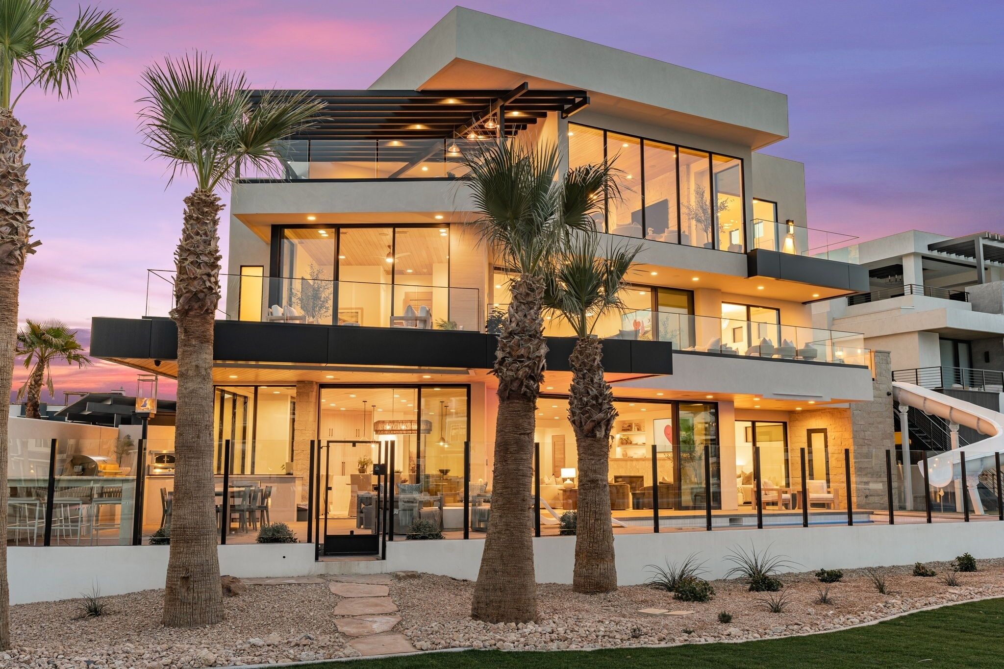 A modern multi-story house with large glass windows, a balcony, and a slide.