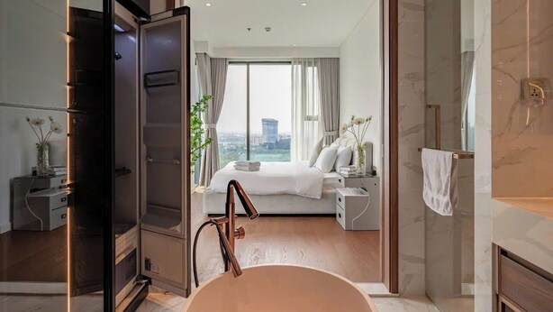 Una habitación de hotel moderna con una cama grande, un baño con bañera y vistas a la ciudad a través de amplias ventanas.