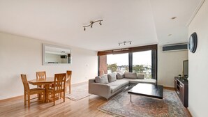 Uma sala de estar moderna com uma mesa de jantar de madeira, sofá bege e uma janela grande com vista para a cidade.