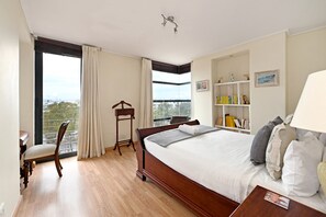 A bedroom with a large bed, a desk, a chair, a bookshelf, and a window with curtains. - Two Bed Spacious 6th Floor Secure (Cape Town)