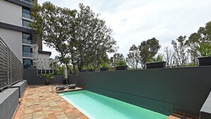 Piscina no terraço com piso de azulejos, rodeada por um muro baixo e vasos de plantas.