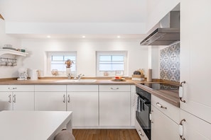 A modern kitchen with white cabinets, a wooden countertop, a built-in oven, and a window with a view. - Cozy Thatched Cottage (Oesterdeichstrich)