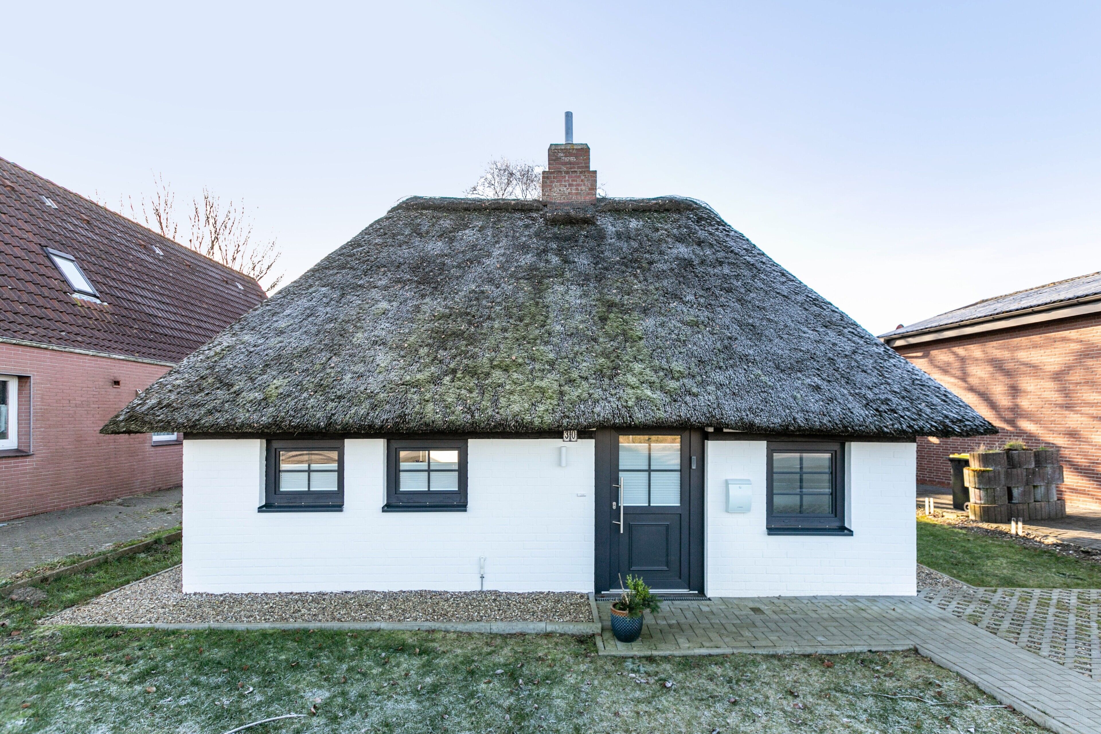 Una piccola casa bianca con tetto di paglia, una porta nera e un'inferriata.
