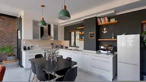 A modern kitchen with white cabinetry, a dining table with chairs, and two pendant lights. - City Center Mountain Views The Piazza (Cape Town)