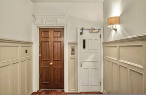 Un couloir avec une porte en bois et une porte blanche, au-dessus de laquelle se trouve un luminaire.