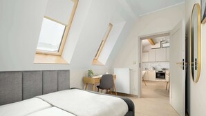 Un dormitorio con techo inclinado, una cama, un escritorio y vistas a la cocina.