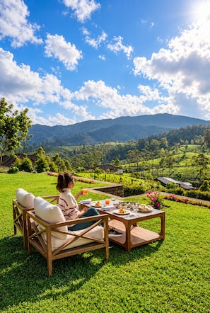Une personne se détend sur un banc en bois, devant une table dressée pour un repas, et profite d’une vue imprenable sur un paysage verdoyant, avec des collines à l’horizon.