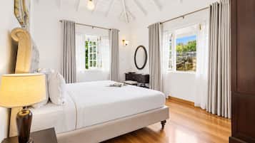 A bedroom with a large bed, a bedside table with a lamp, a dresser, a mirror, and a window with curtains.