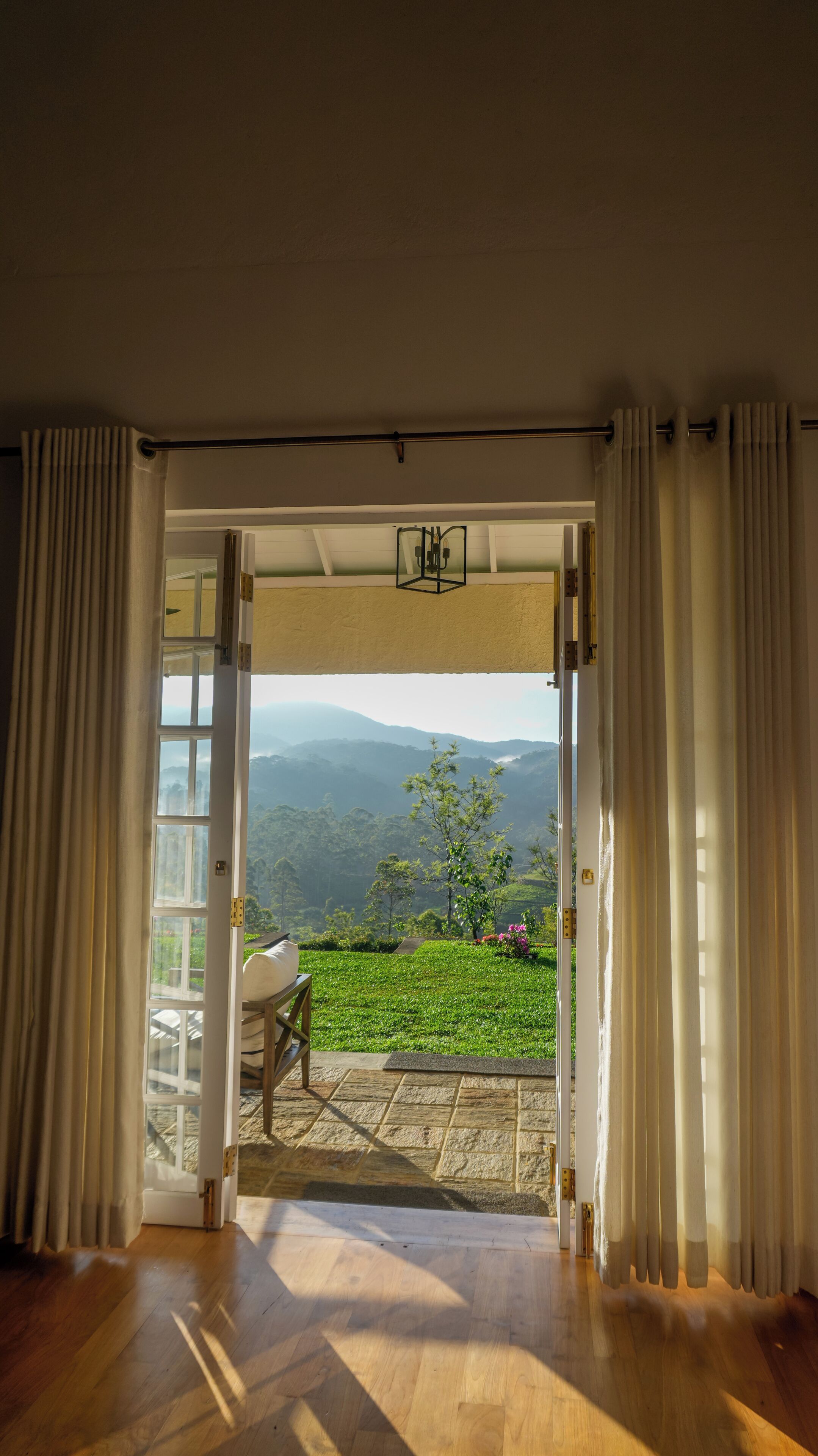 Un umbral abierto que da a un balcón con vistas a montañas y vegetación.