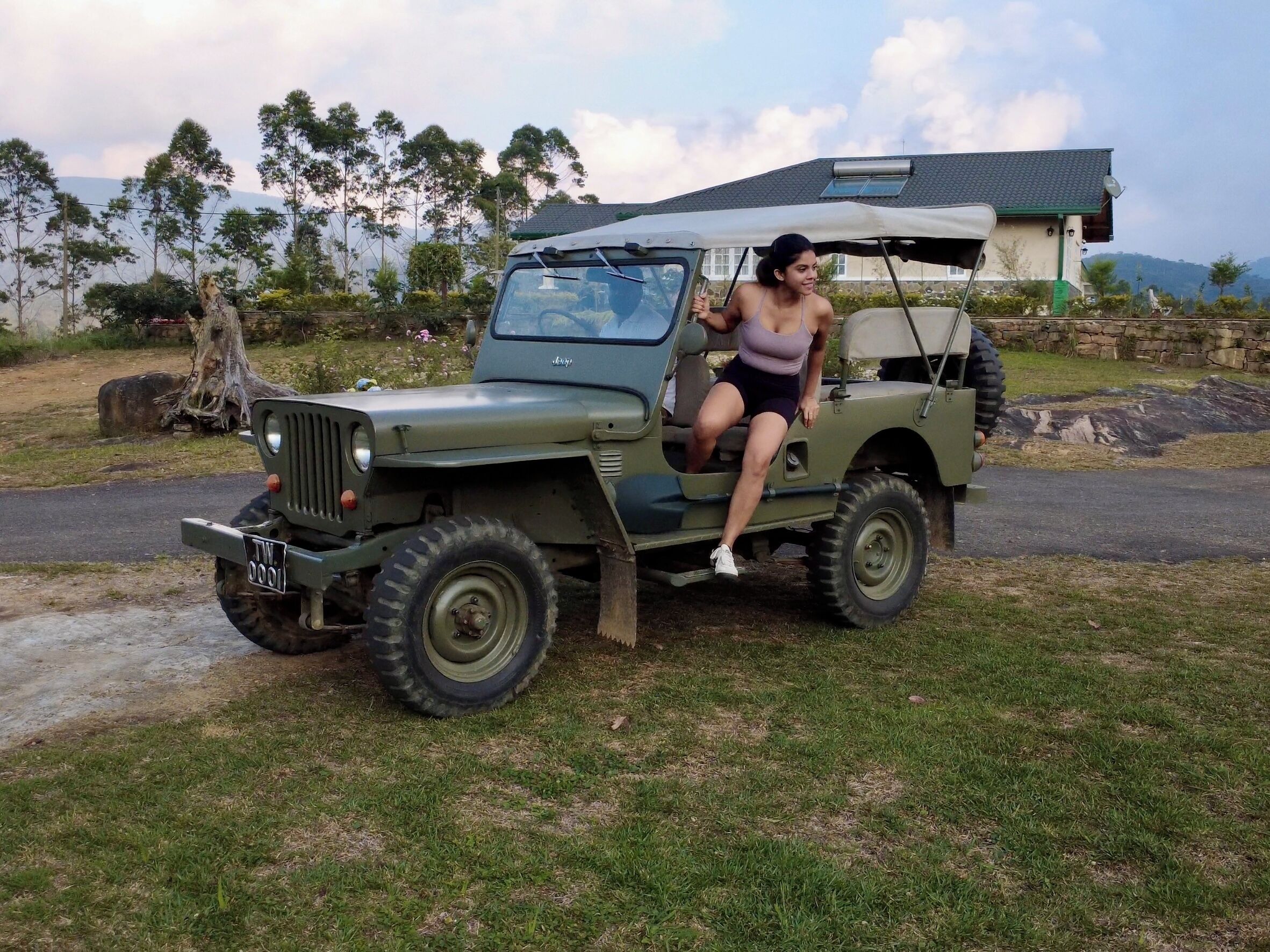 A military-style vehicle parked on a grassy area with a house in the background.