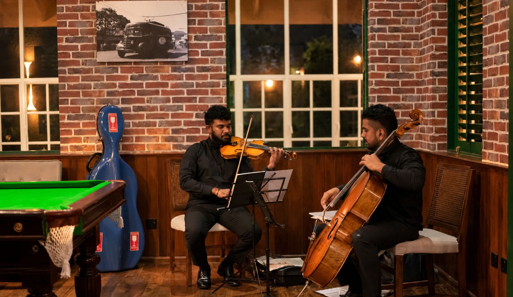 A room with a pool table, a violinist, and a cellist playing music.