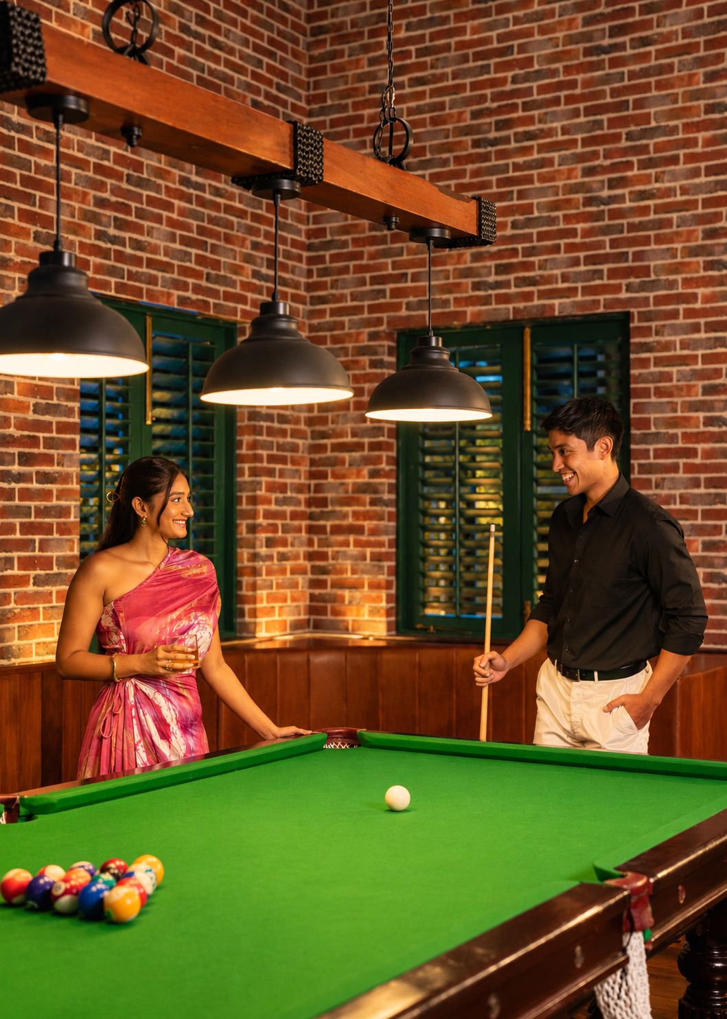 A billiards table with balls and a cue stick, a person in a pink dress, and another in a black shirt.