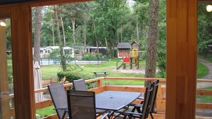 Terraza al aire libre con mesa y sillas, con vista a un parque infantil y una piscina.