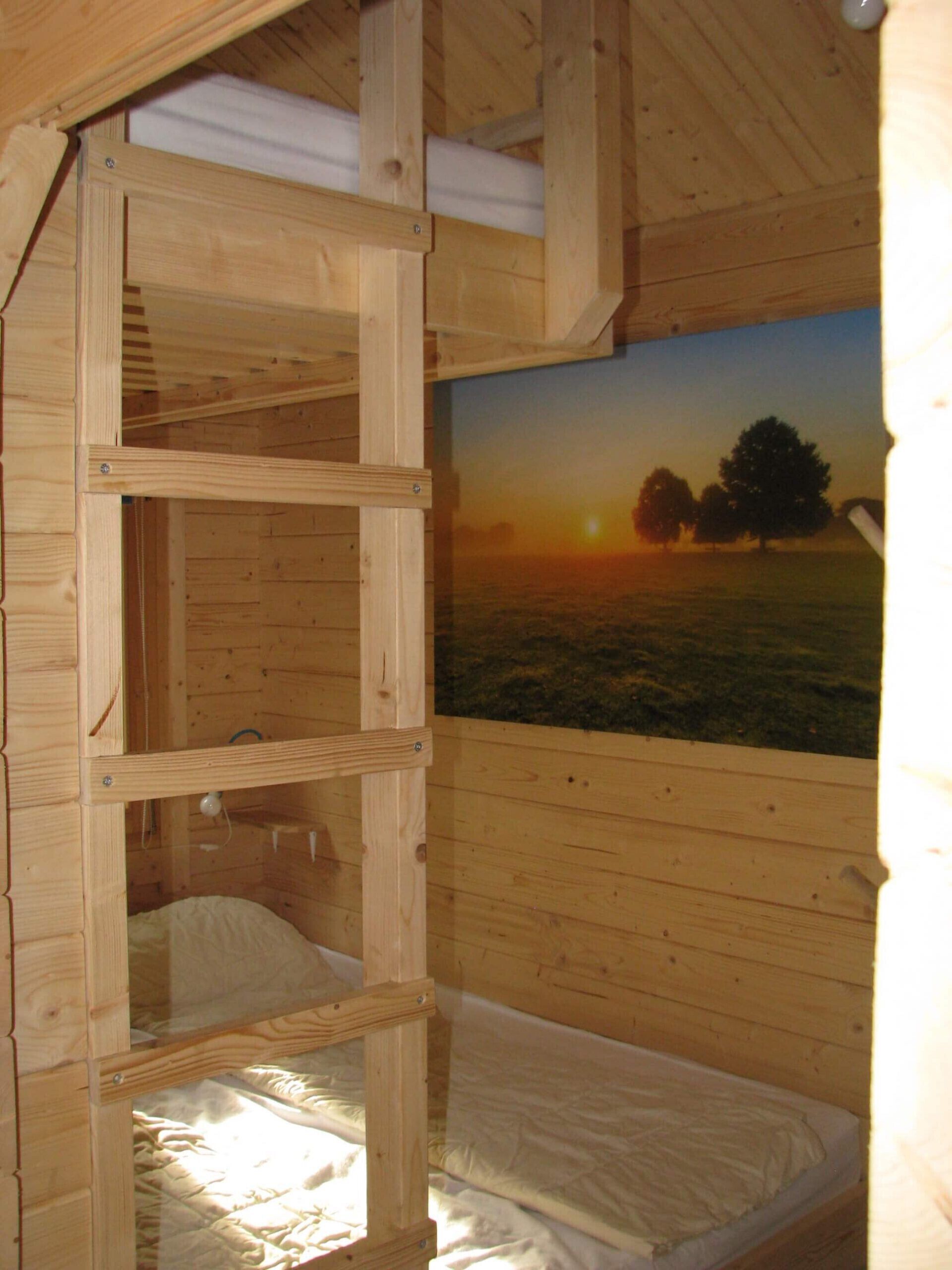 Quarto de cabana de madeira com beliche, uma pintura de um pôr do sol e uma escada.