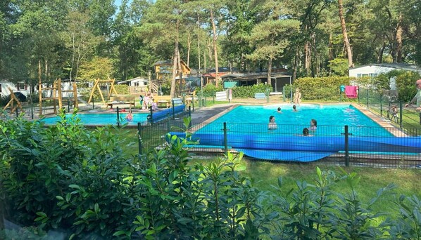 Ett poolområde med flera pooler, omgivet av träd och en lekplats.
