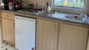 Cuina compacta amb armaris de fusta, rentaplats integrat, finestra amb vista a la vegetació i taulell amb diversos objectes.