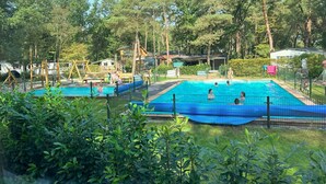 Zona de piscines amb diverses piscines, envoltada d'arbres i un parc infantil.