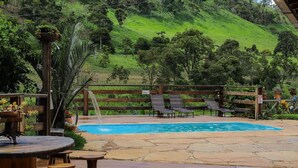 A pool area with a wooden fence, lounge chairs, and a view of a green hillside. - S tio Toca dos Gatos com Piscina e Churrasqueira (Sabinópolis)