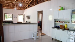 A kitchen with white cabinets, a black countertop, and a stool. There is a window with a view of greenery outside. - S tio Toca dos Gatos com Piscina e Churrasqueira (Sabinópolis)