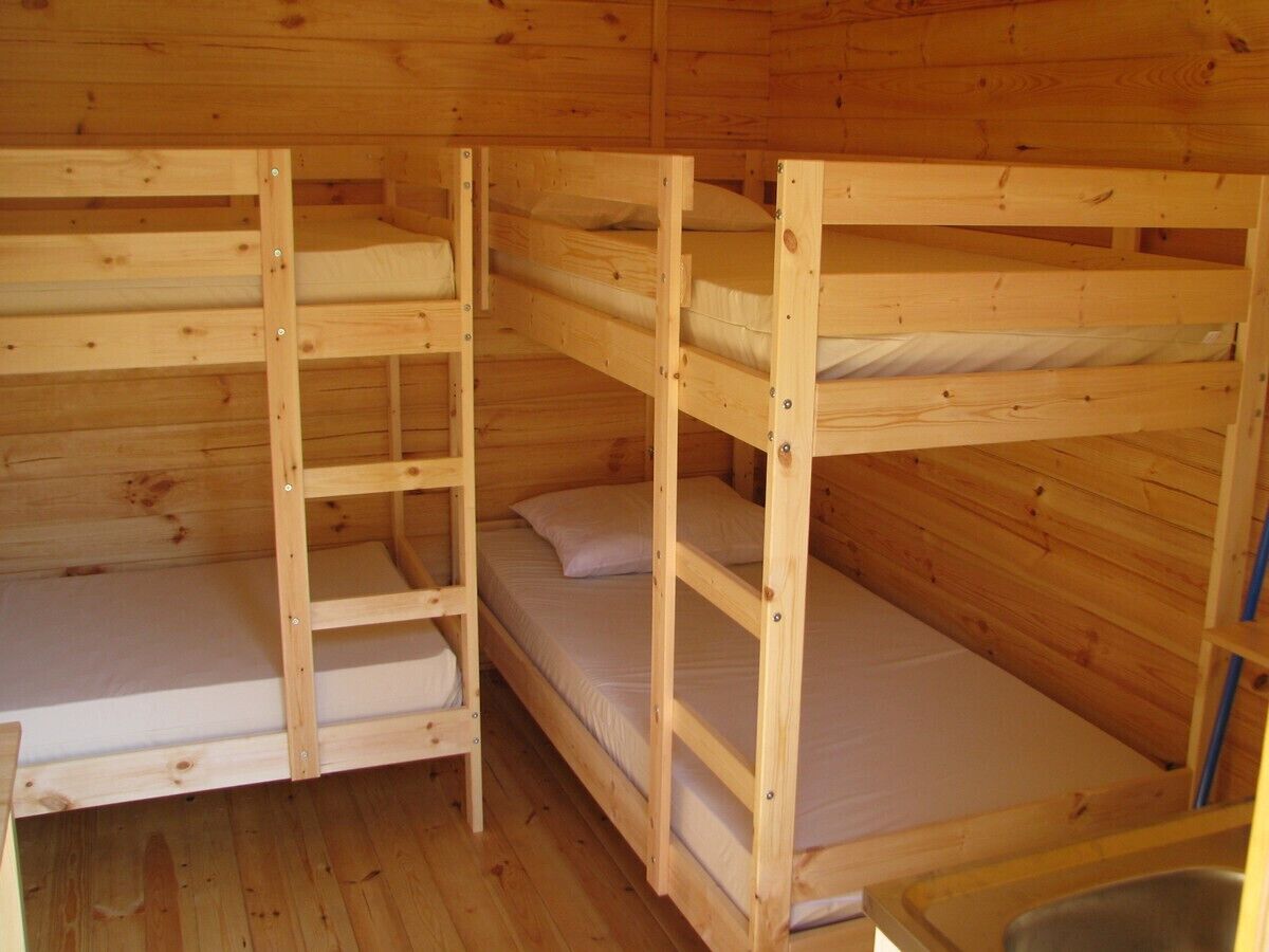 Una cabaña de madera con literas, piso de madera y un lavamanos de metal.